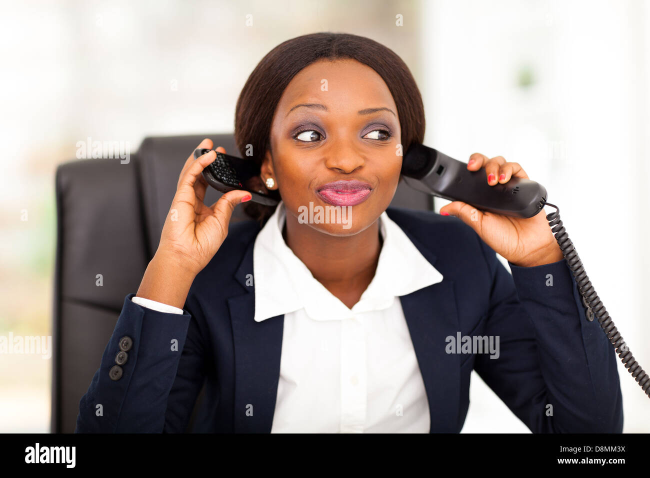 Funny African American femmina di lavoratore di ufficio parlando su telefoni fissi e cellulari allo stesso tempo Foto Stock