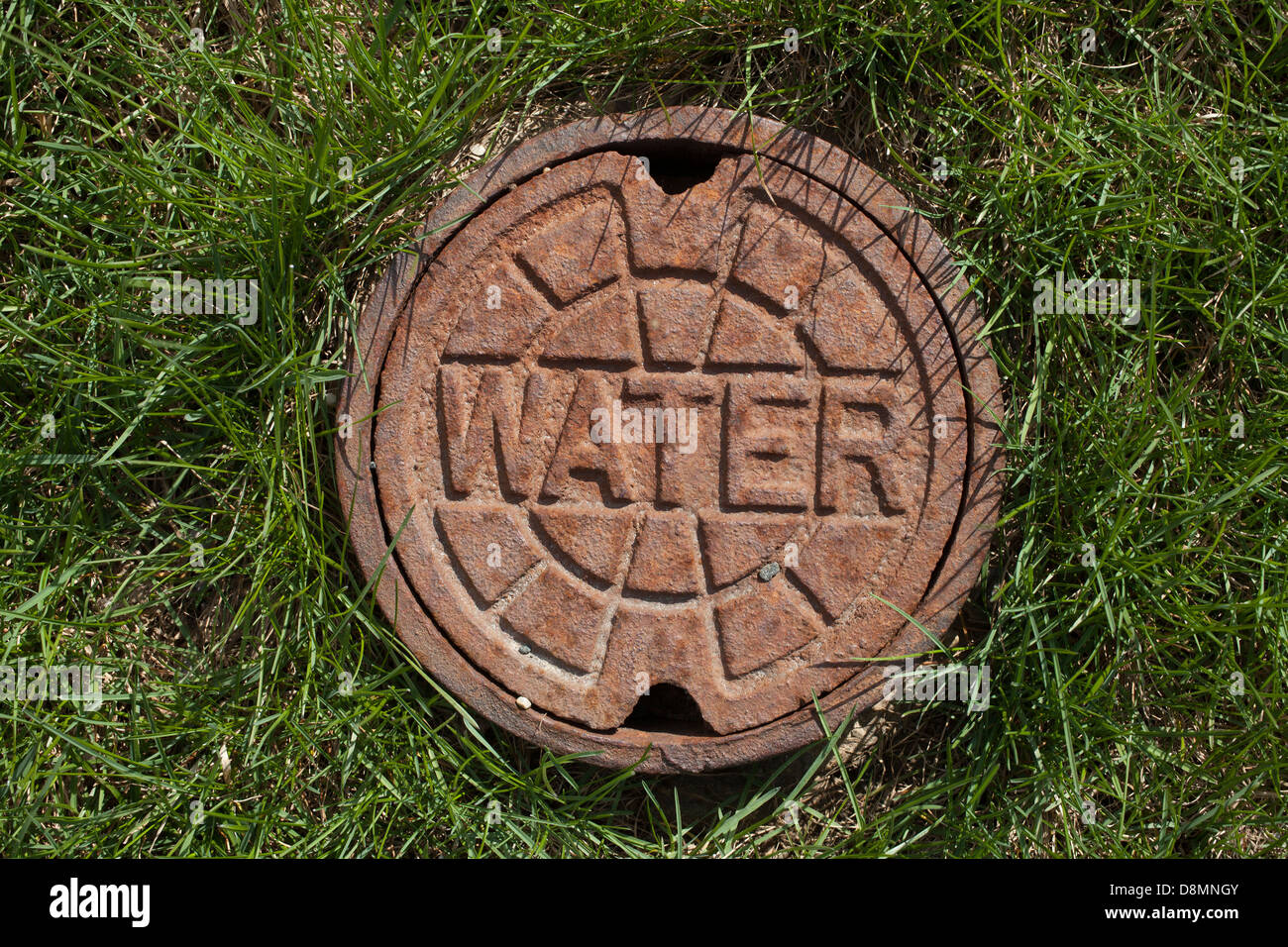 Una piccola utility acqua ghisa coperchio è impostato nel prato. Foto Stock