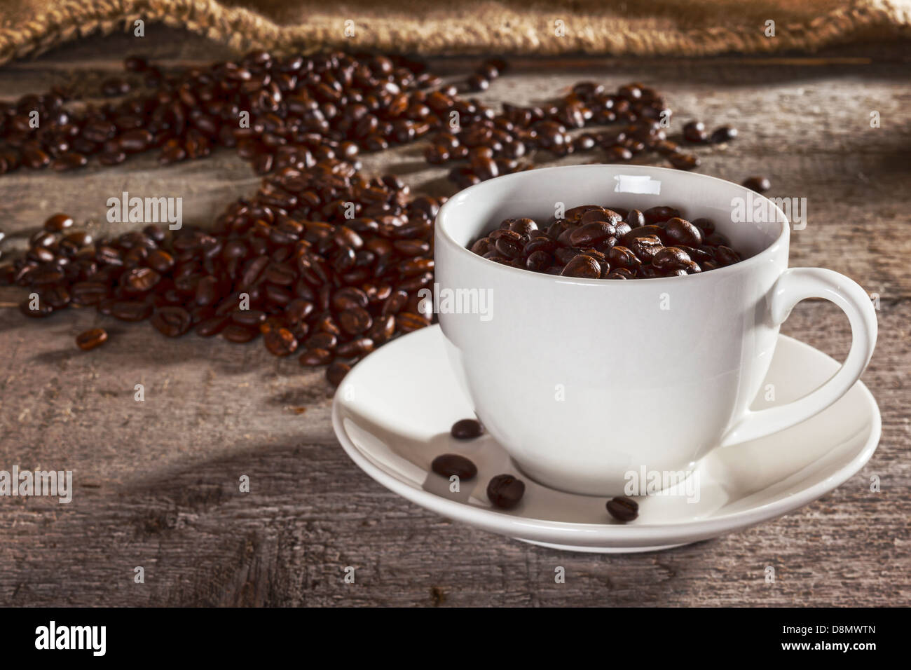 I chicchi di caffè e rustico sfondo - tazza da caffè con piattino riempito con i chicchi di caffè, con i chicchi di caffè e tela sacco dietro... Foto Stock