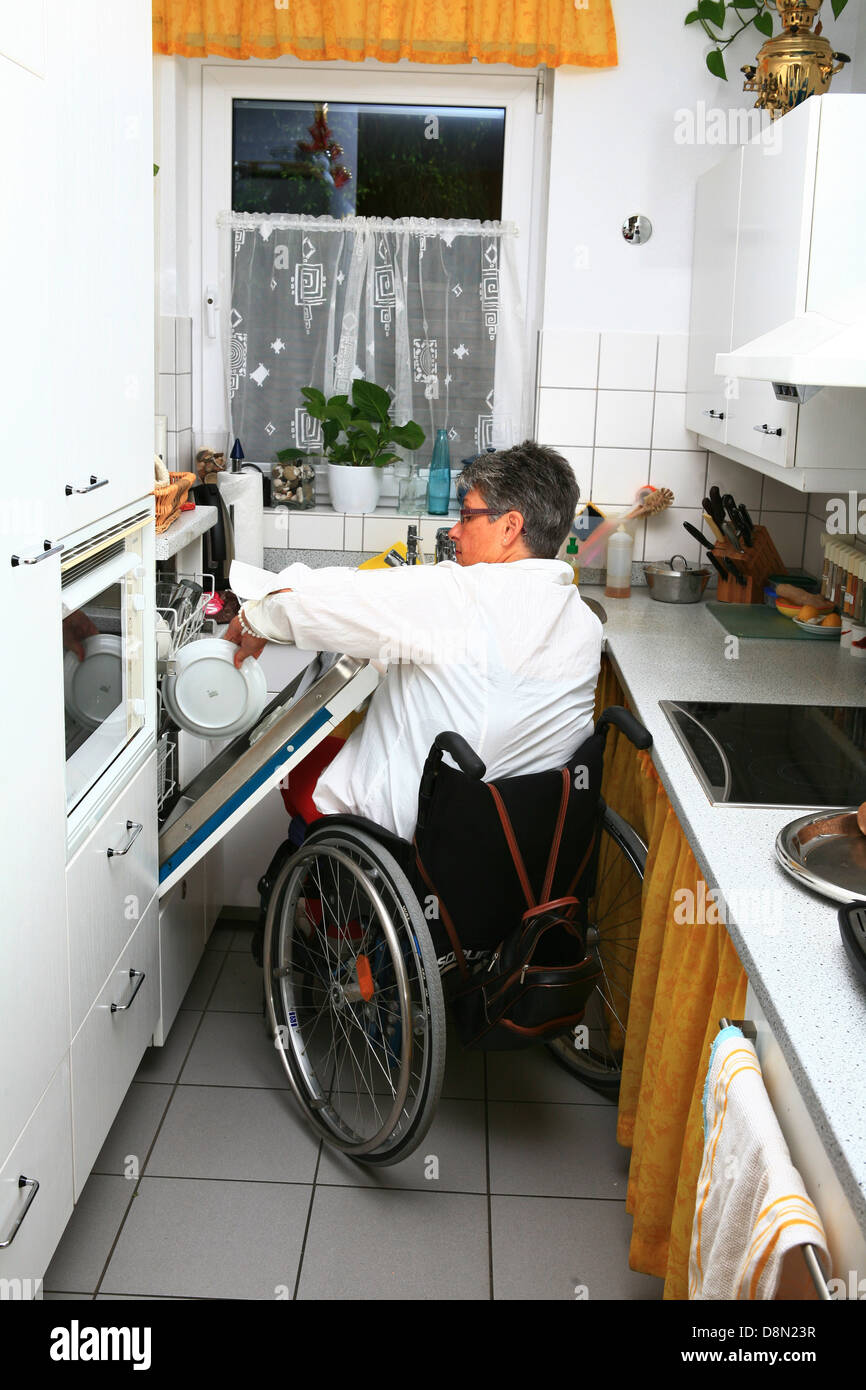 Una donna su una sedia a rotelle in cucina Foto Stock