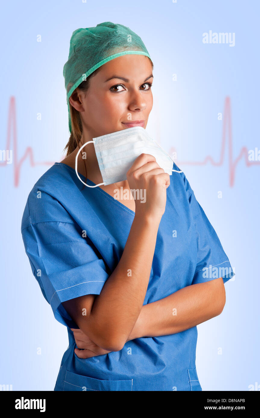 Giovani donne chirurgo con scrubs, tenendo una maschera per il viso con un grafico EKG dietro di lei Foto Stock