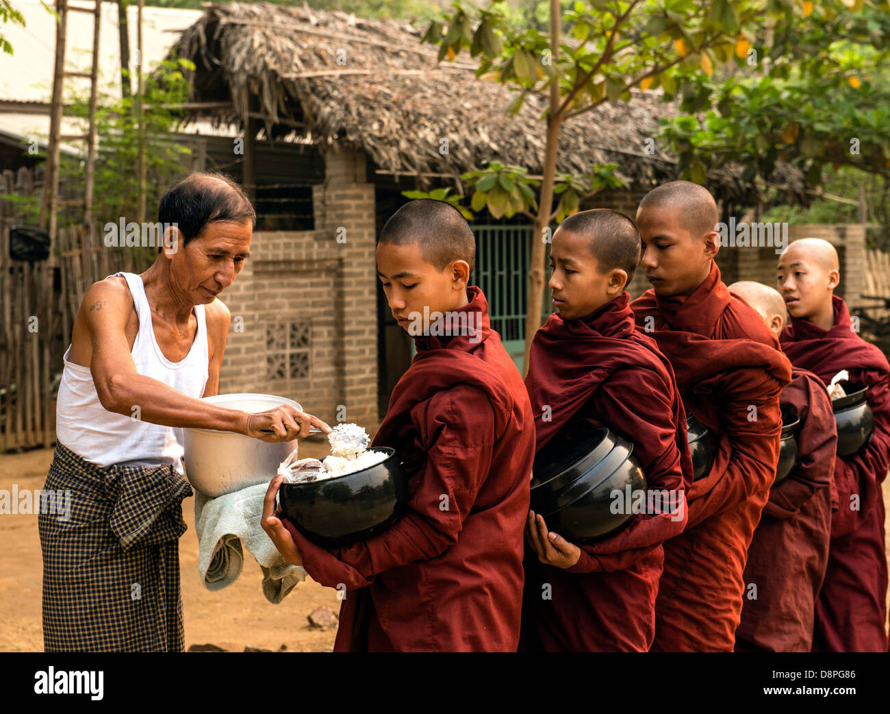 I monaci buddisti raccogliendo elemosine ciotole di cibo al mattino da abitanti di un villaggio vicino a Bagan Birmania Myanmar Foto Stock