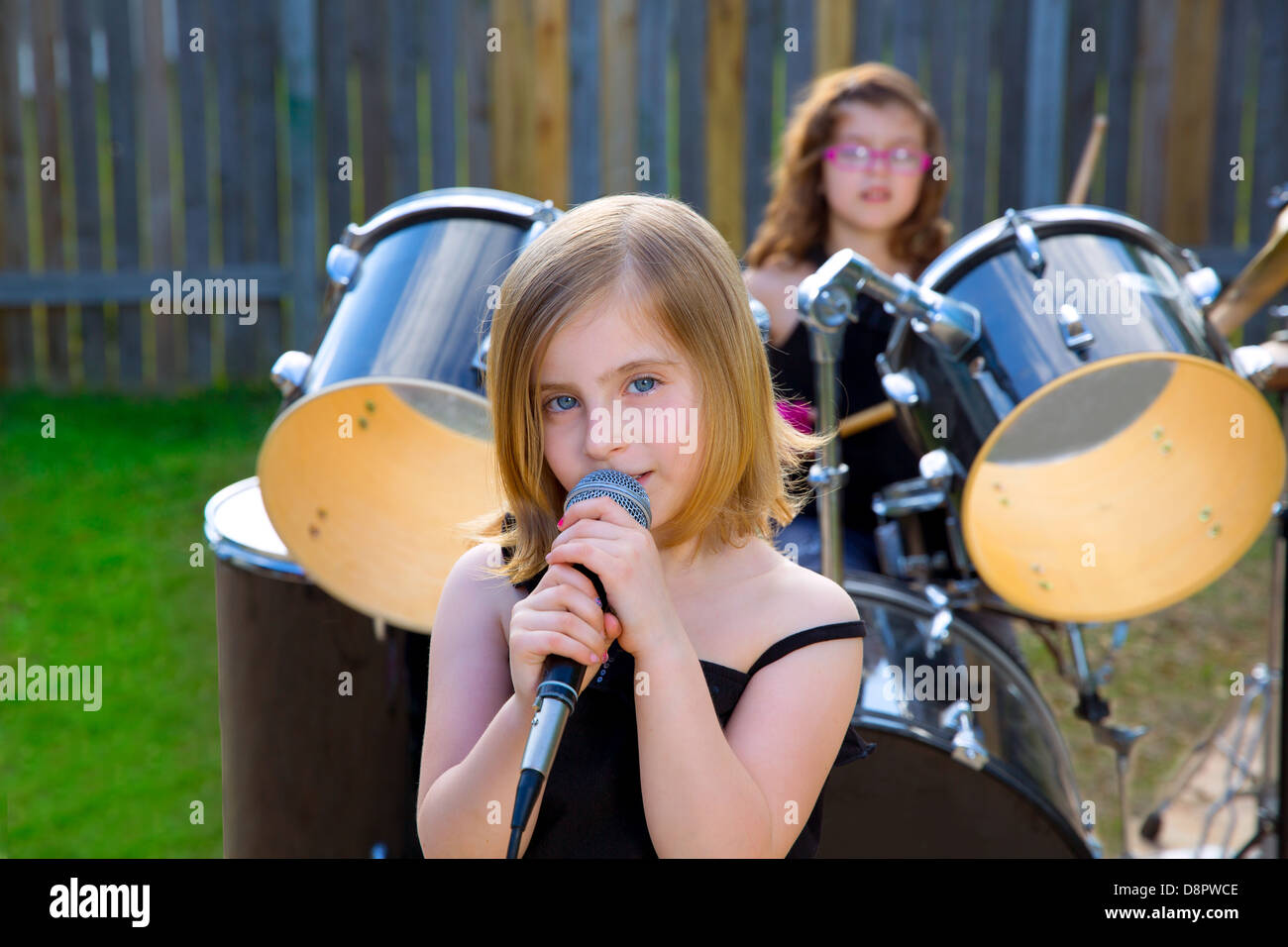 Blonde kid ragazza cantando in tha backyard con tamburi dietro Foto Stock