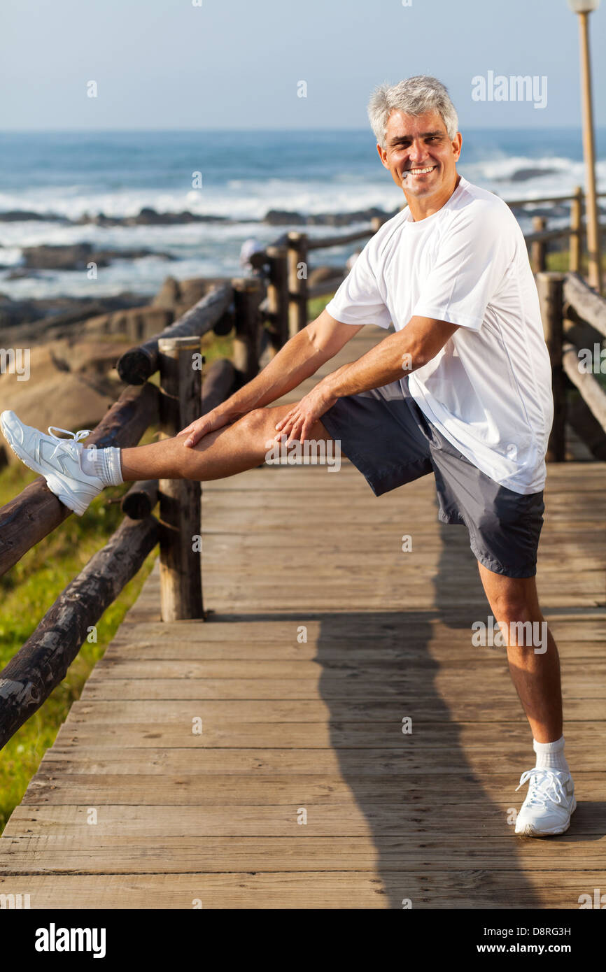 Active uomo maturo stretching gamba la mattina in spiaggia Foto Stock