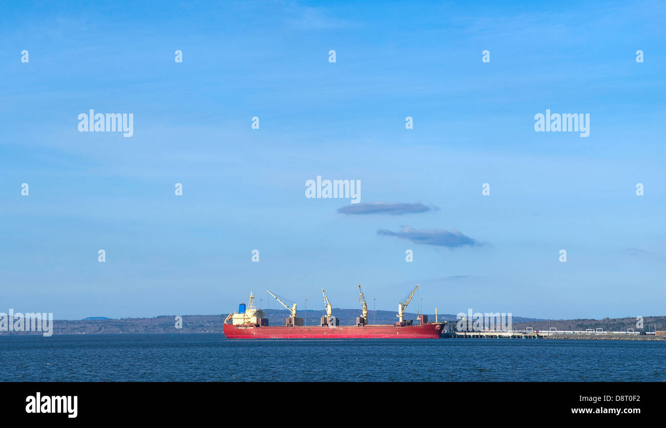 Una grande nave da carico con un rosso scafo e sovrastrutture bianco ancorata ad un molo commerciale. Foto Stock