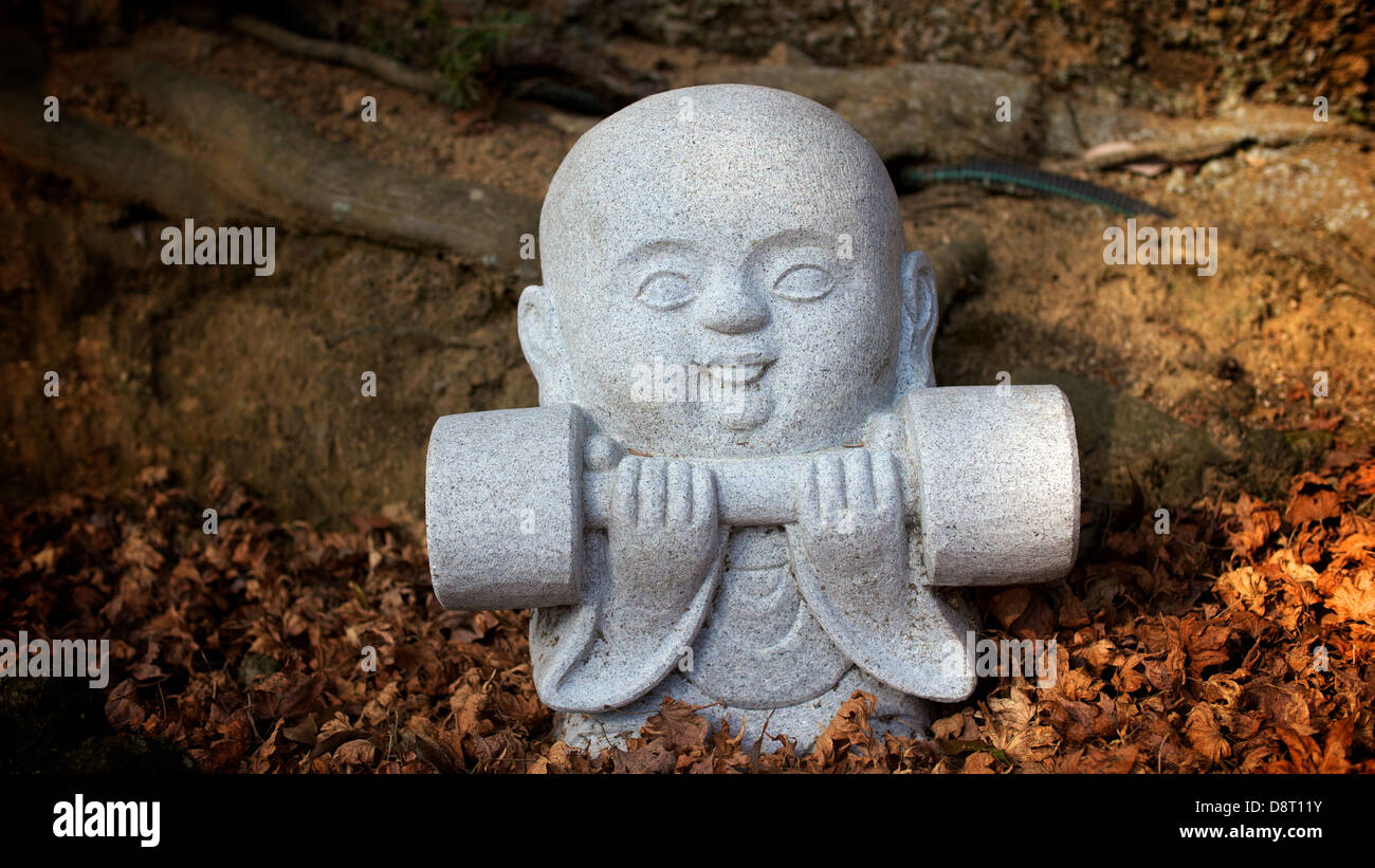 Piccola statua di pietra di un po' di Monaco il sollevamento di un peso al Tempio Daishoin in Miyajima Foto Stock