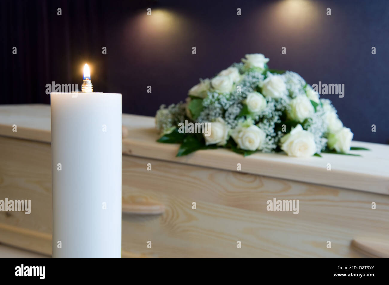 Una candela che brucia con una bara e un omaggio floreale sullo sfondo in una camera mortuaria Foto Stock