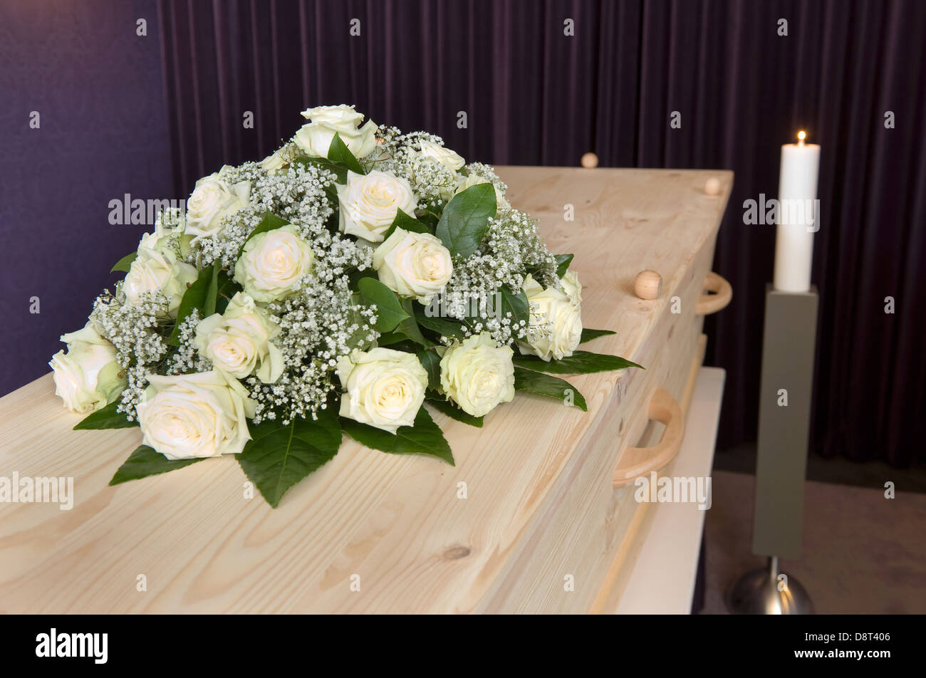 Un omaggio floreale in una bara e una candela che brucia sullo sfondo in una camera mortuaria Foto Stock