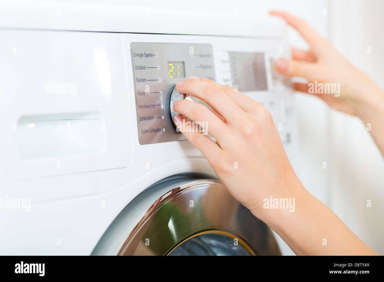 Giovane donna o governante dispone di un servizio lavanderia giorno a casa, si seleziona il programma Foto Stock