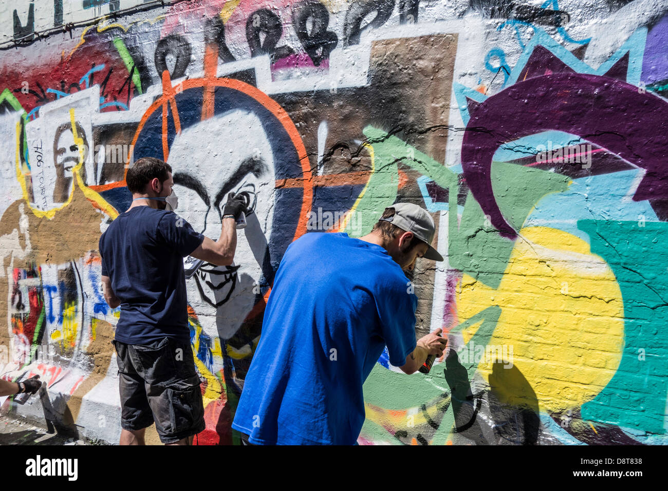 Ragazzi con bombolette spray in vicolo spruzzatura coloratissimo graffito sulla parete dell'edificio della città Foto Stock