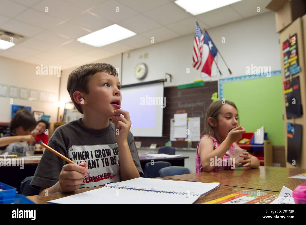 7 anno vecchio ragazzo Mexican-American siede in prima elementare Scuola elementare classe e scrive in notebook con una matita Foto Stock