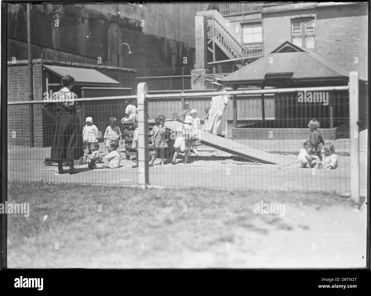 Una storica fotografia in bianco e nero del Lance Playground a Millers Point, Sydney, scattata all'inizio del XX secolo. L'immagine mostra i bambini in gioco, illustrando lo sviluppo dell'area come parte delle iniziative comunitarie del Sydney Harbour Trust. La foto è conservata negli archivi del NSW della State Records. Foto Stock