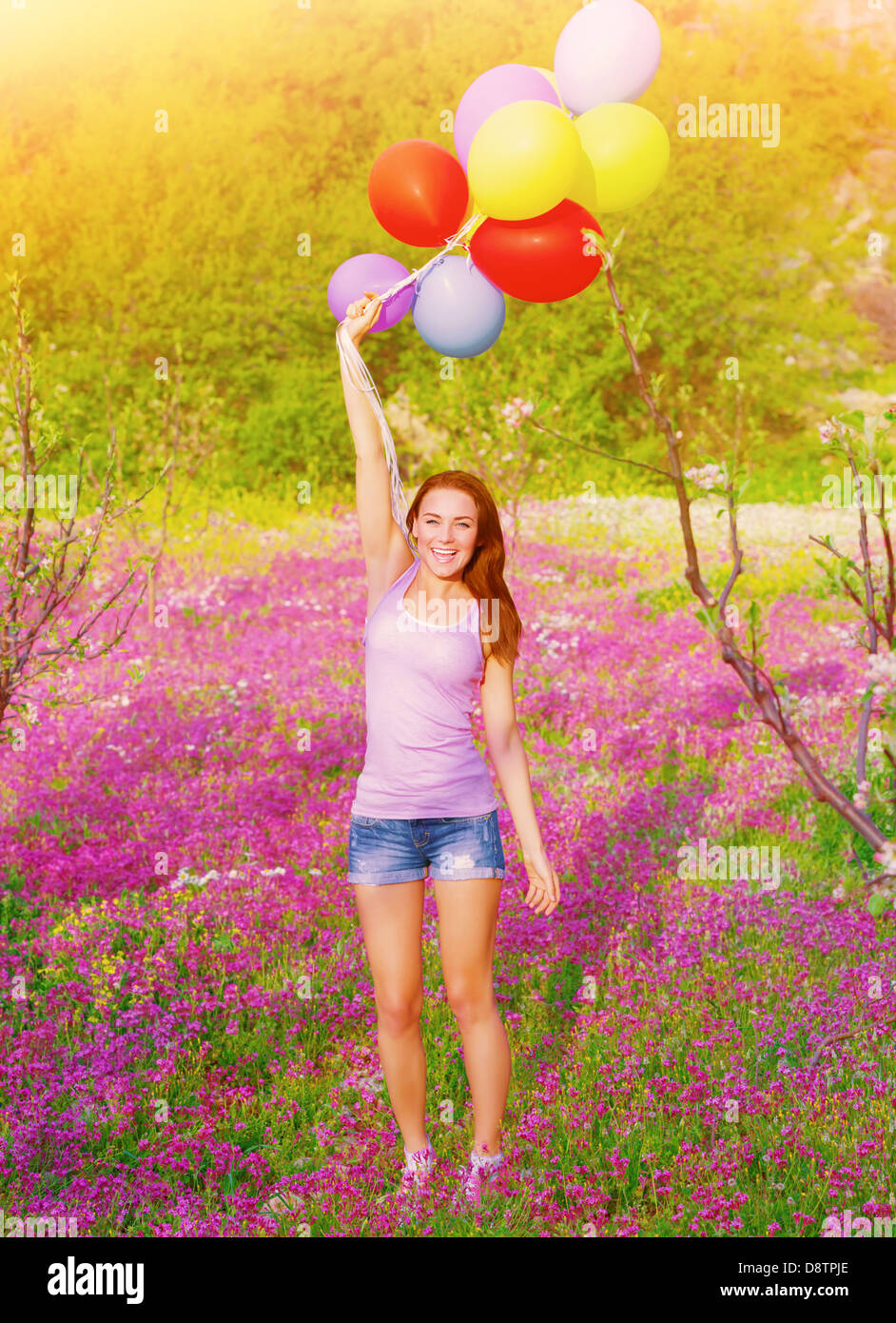 Felice giovane donna tenendo in mano molti palloncini colorati, divertirsi su viola campo floreale, Estate stagione Foto Stock