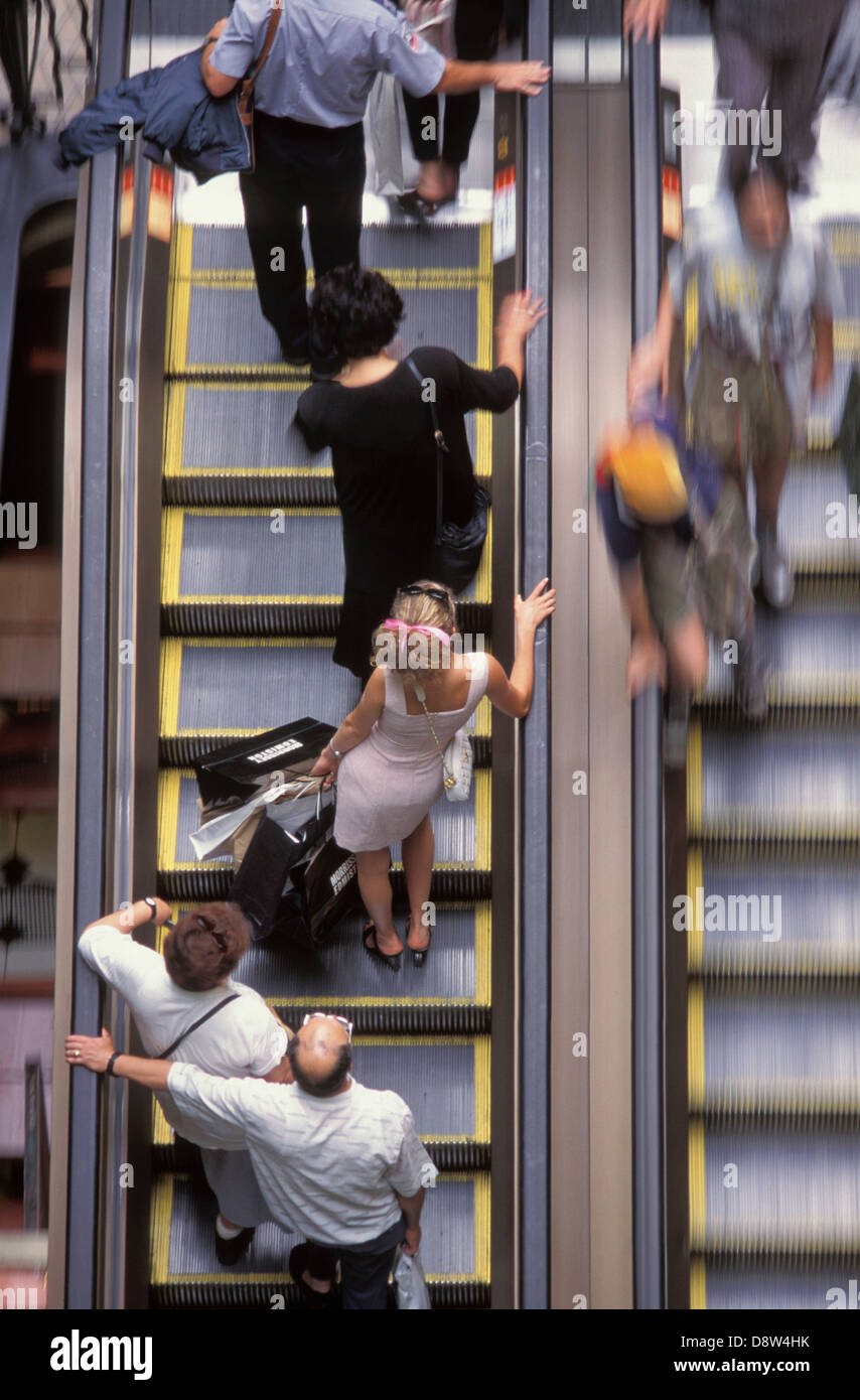 Donna che indossa abiti rosa e nastro rosa tra i capelli, vista posteriore, il trasporto delle borse della spesa sulla affollata escalator, Sydney, Australia Foto Stock