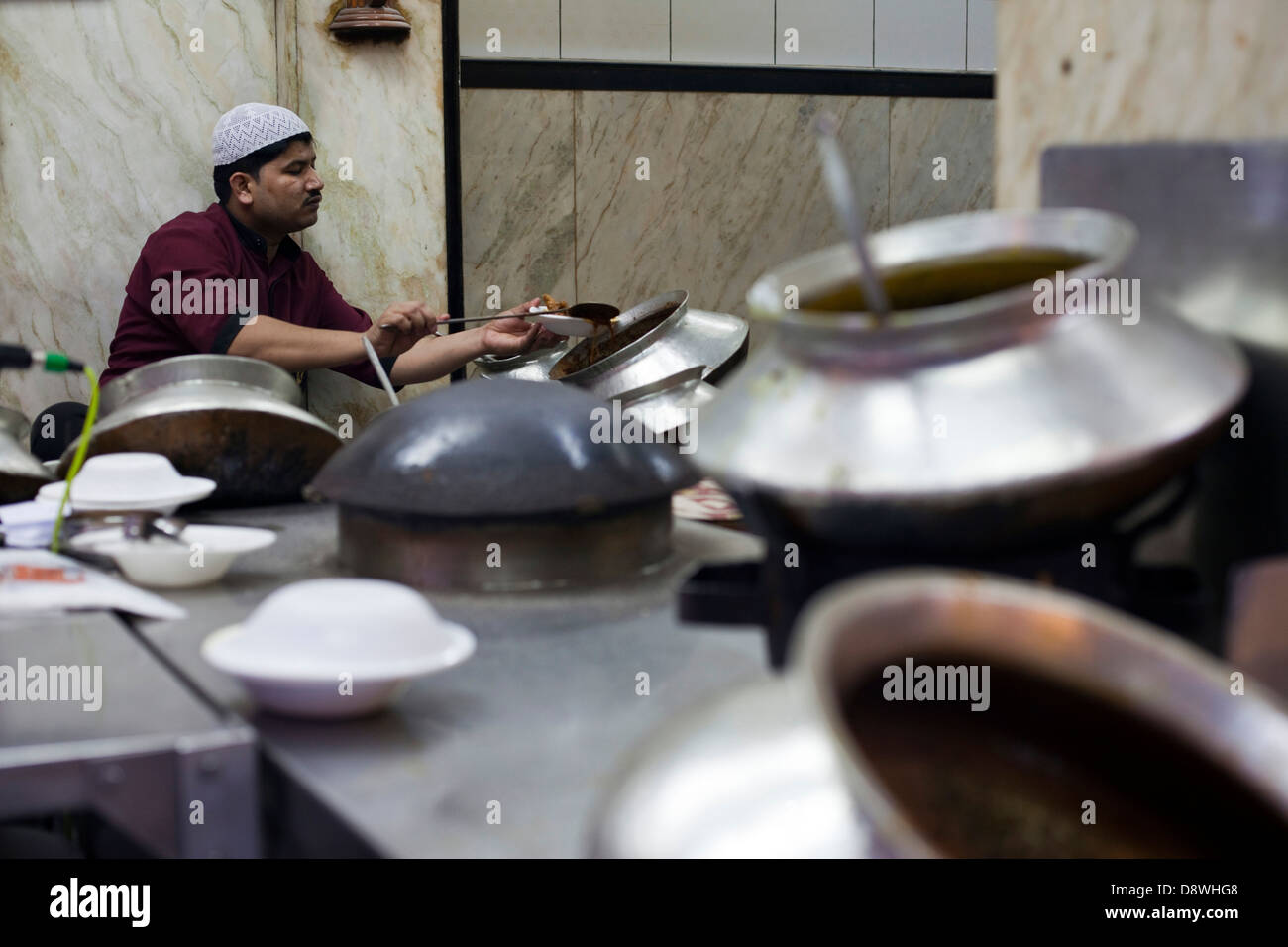 Un uomo serve curry dalla enormi vasi nel cortile al Ristorante Karims, Vecchia Delhi Foto Stock