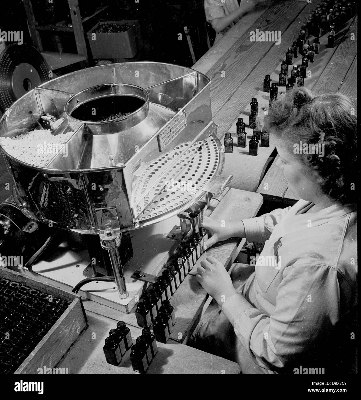 Storico degli anni cinquanta. Inghilterra. farmaci. Femmina operativa in fabbrica su una linea di produzione di bottiglie di pillole o compresse. Foto Stock