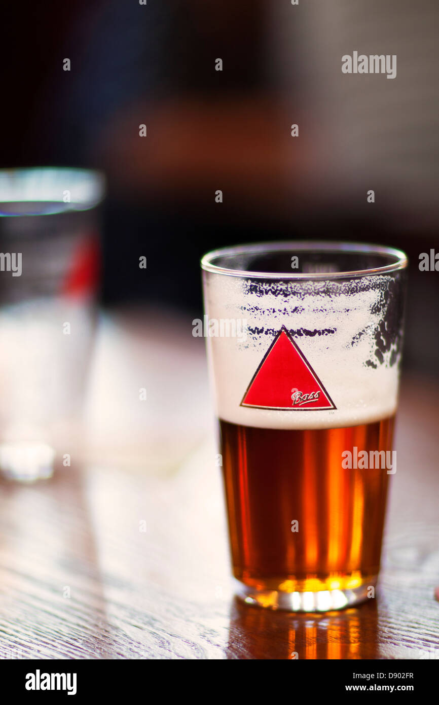 Bicchiere mezzo pieno...una mezza pinta di birra Bass in una pinta di vetro in un pub inglese su una tavola di legno Foto Stock