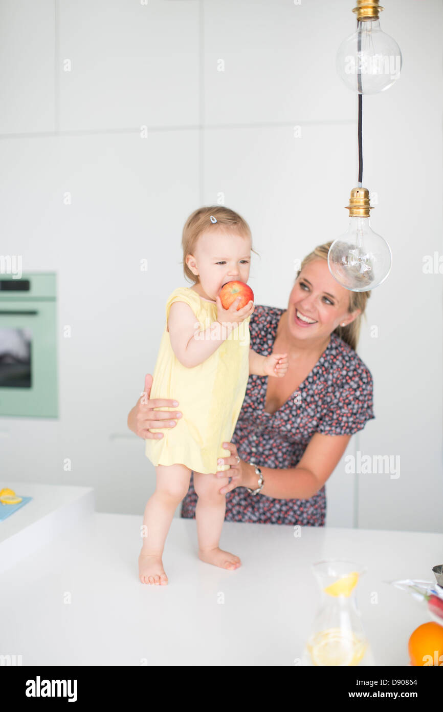 Little Girl eating apple mentre la madre che abbraccia il suo Foto Stock