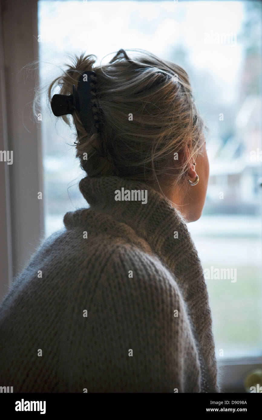 Una giovane donna che guarda fuori da una finestra. Foto Stock