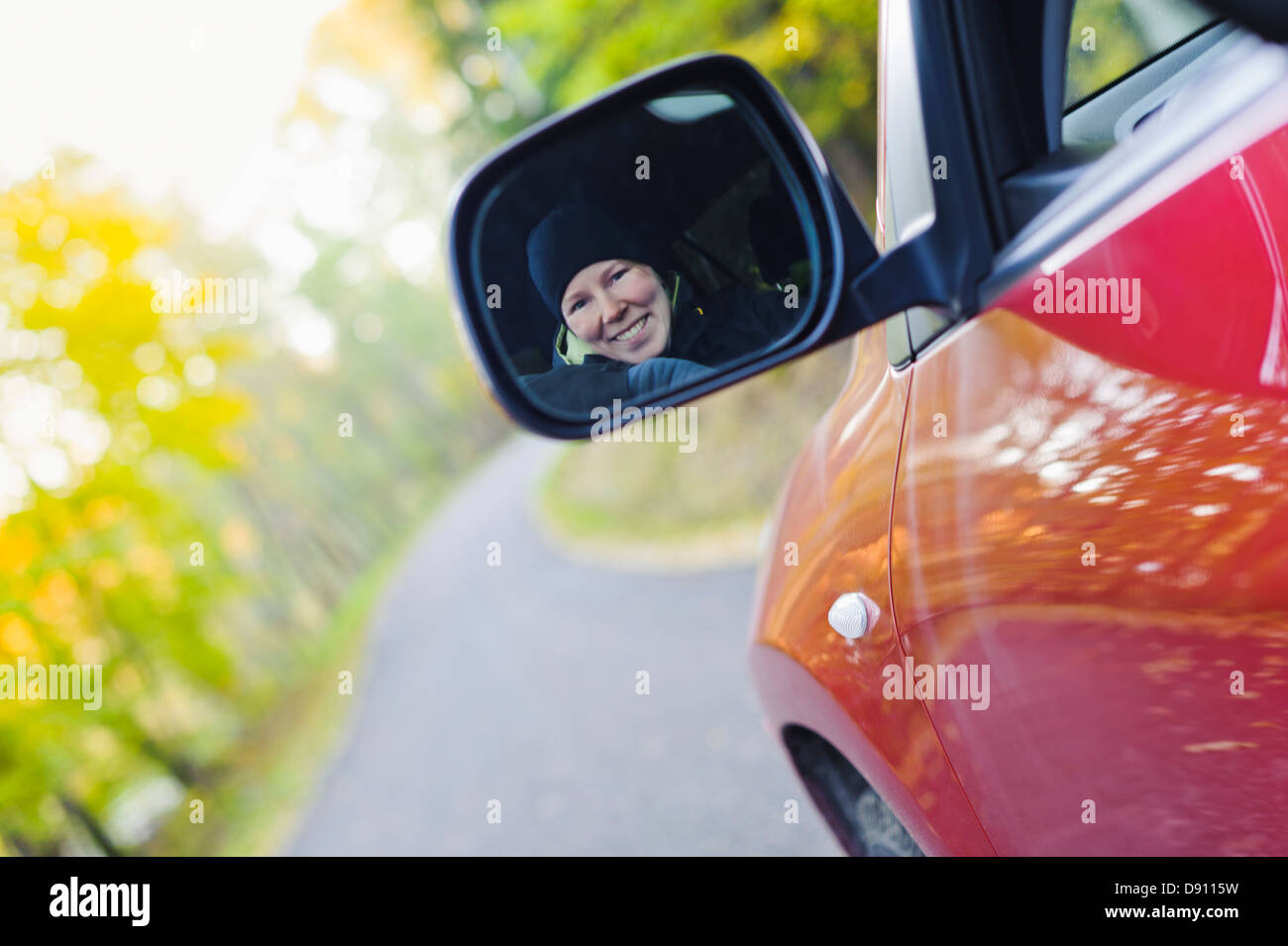 Donna sorridente in specchio retrovisore sulla strada di campagna Foto Stock