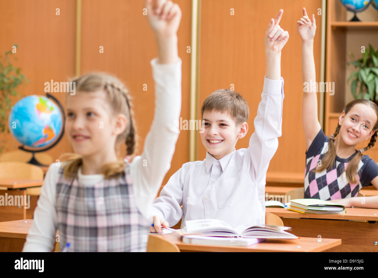 La scuola dei bambini con le mani alzate a lezione in aula Foto Stock
