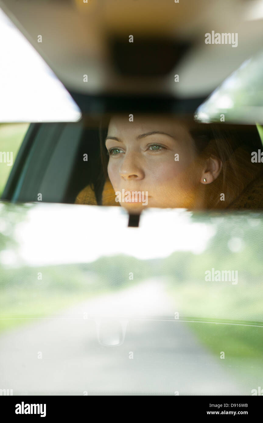 Giovane donna alla guida di auto riflettendo a specchio retrovisore Foto Stock