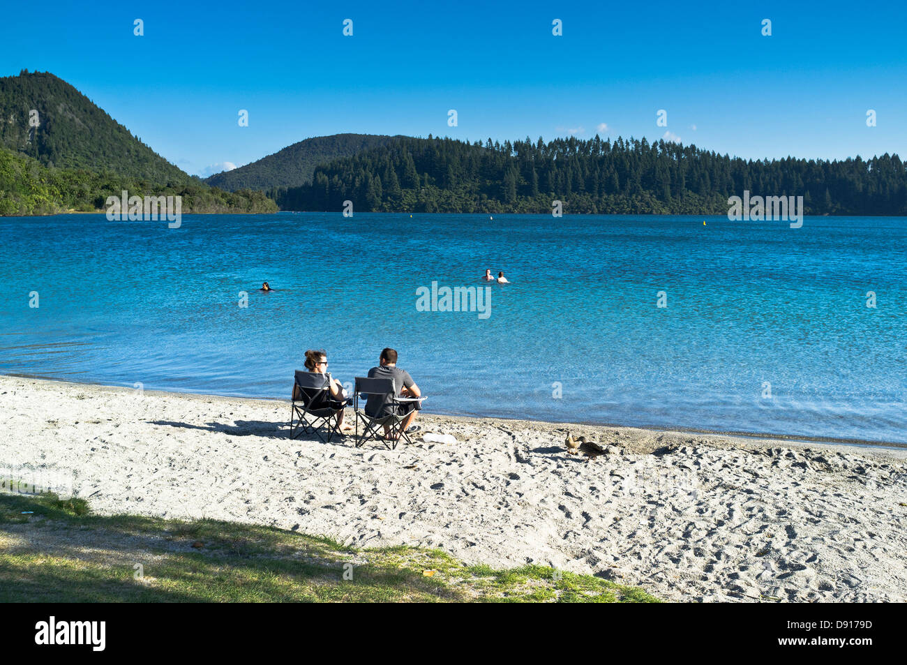 dh Blue Lake ROTOROA NUOVA ZELANDA coppia seduta sulla spiaggia di sabbia lago Tikitapu vacanza Foto Stock