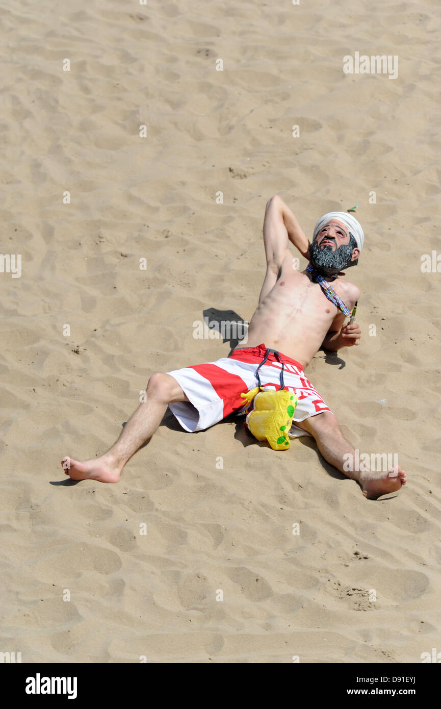 Porthcawl, South Wales, Regno Unito 8 Giugno 2013. Il clima caldo attrae folle di Porthcawl beach in Galles del sud su uno dei giorni più caldi dell'anno. Un giovane uomo sunbathes con un Osama Bin Laden sulla maschera a Porthcawl beach. Credito: Matteo Horwood/Alamy Live News Foto Stock