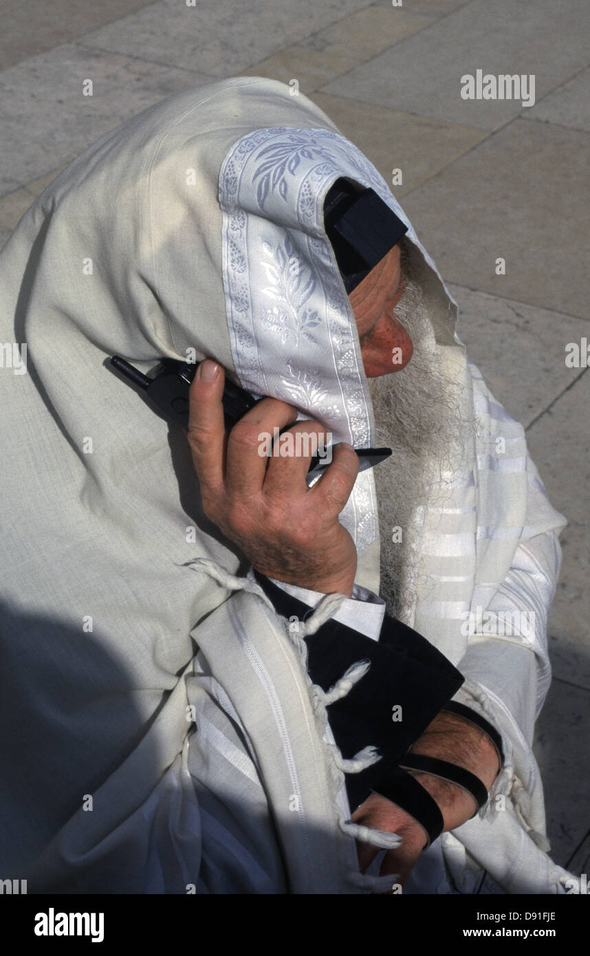 Una religiosa ebraica uomo avvolto con scialle Talit usando un vecchio telefono cellulare nella parete occidentale della città vecchia di Gerusalemme Israele Foto Stock