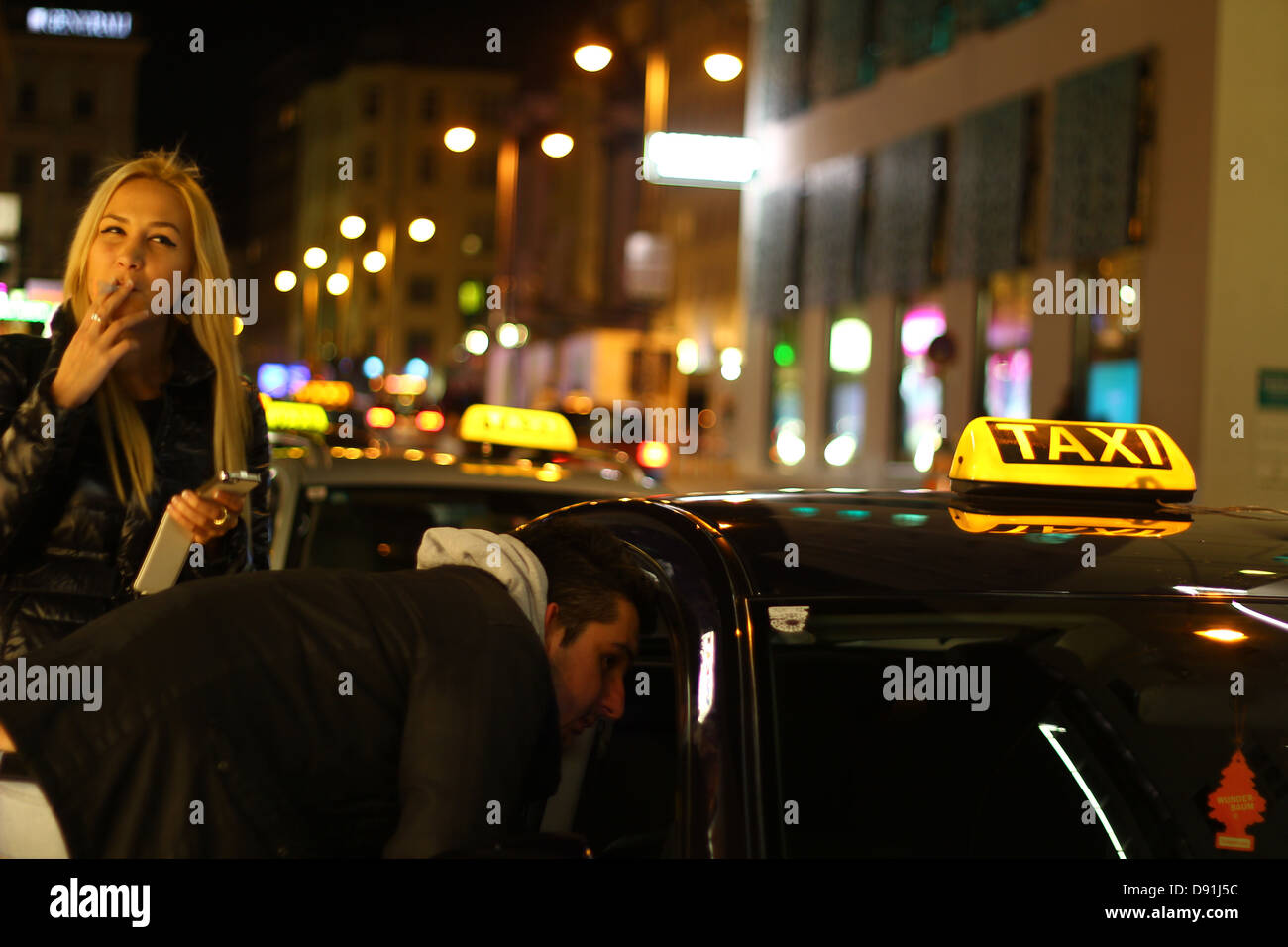 Scena di vita notturna di Vienna - coppia giovane da un taxi auto : sta negoziando un prezzo, lei è il fumo durante l'attesa, Austria Foto Stock