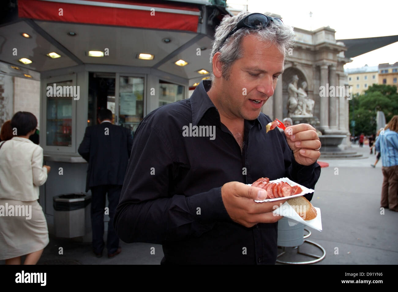 L'uomo mangiare kasewurst (salsiccia contenente formaggio) da un wurstelstand (salsiccia stand) nel centro di Vienna, Austria Foto Stock