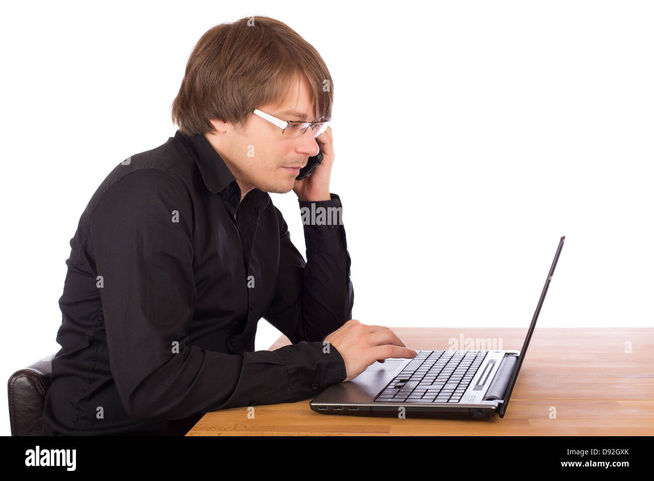 Giovane uomo d affari con camicia nera e il telefono cellulare a lavorare seriamente su un laptop. Isolato su sfondo bianco. Foto Stock