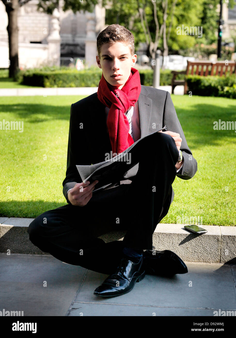 Un giovane imprenditore tenendo un giornale mentre seduto in un parco Foto Stock
