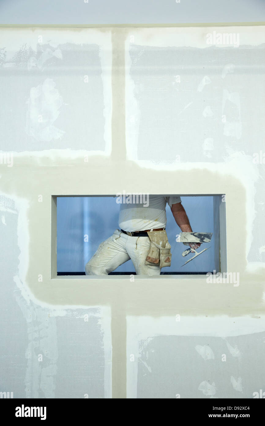 Un imbianchino tenendo una cazzuola, visto attraverso la finestra foro in una nuova parete costruito Foto Stock