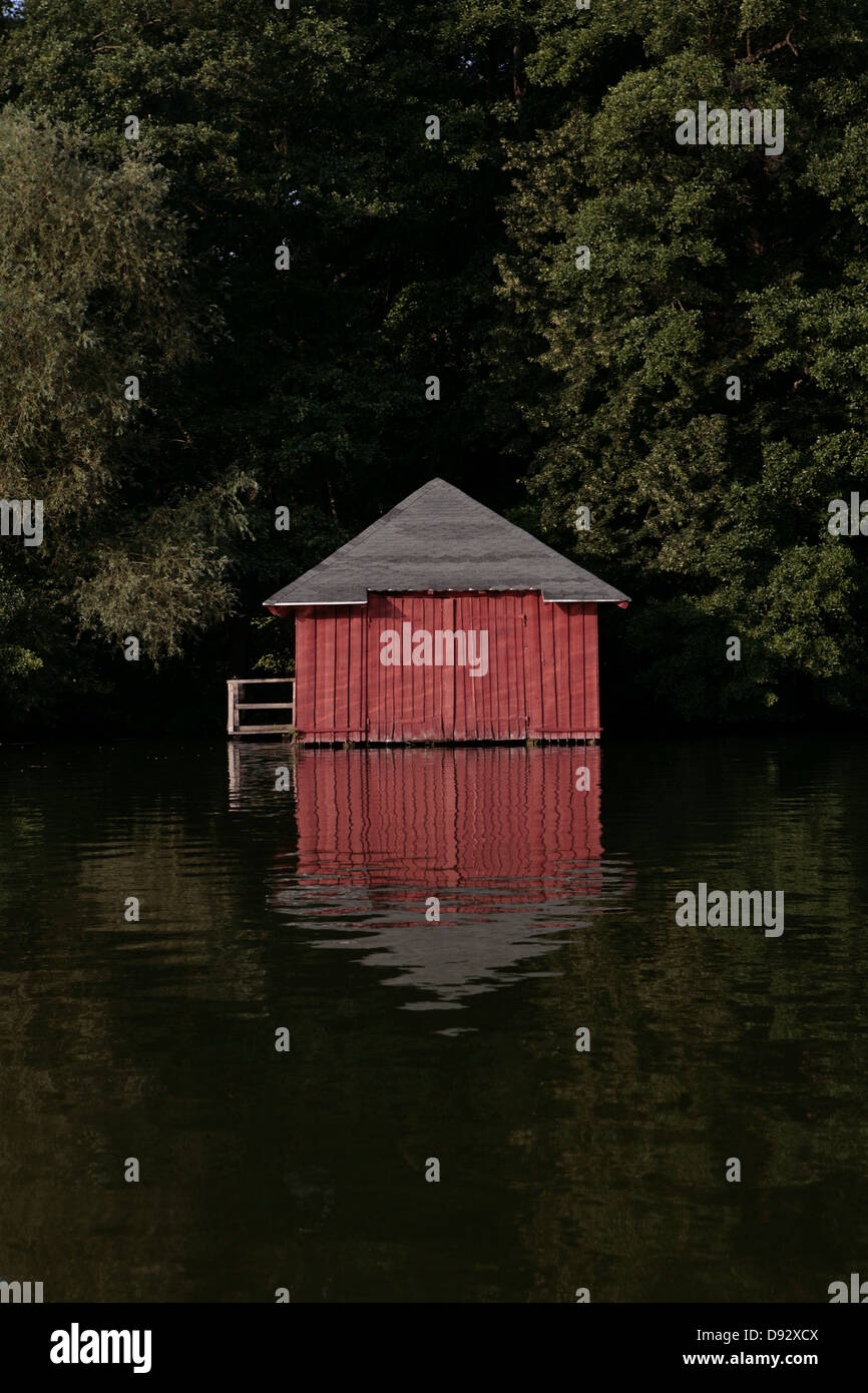 Un rosso boathouse accoccolato tra alberi sulle sponde di un lago. Foto Stock