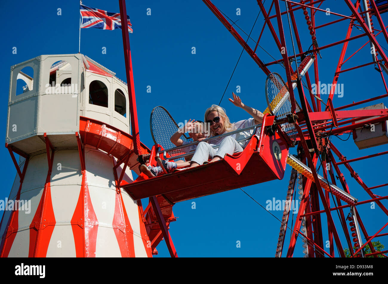 Madre e figlio giovane sventolare su una ruota panoramica Ferris ride, contro un cielo azzurro, a una fiera estiva in Inghilterra, Regno Unito. Foto Stock