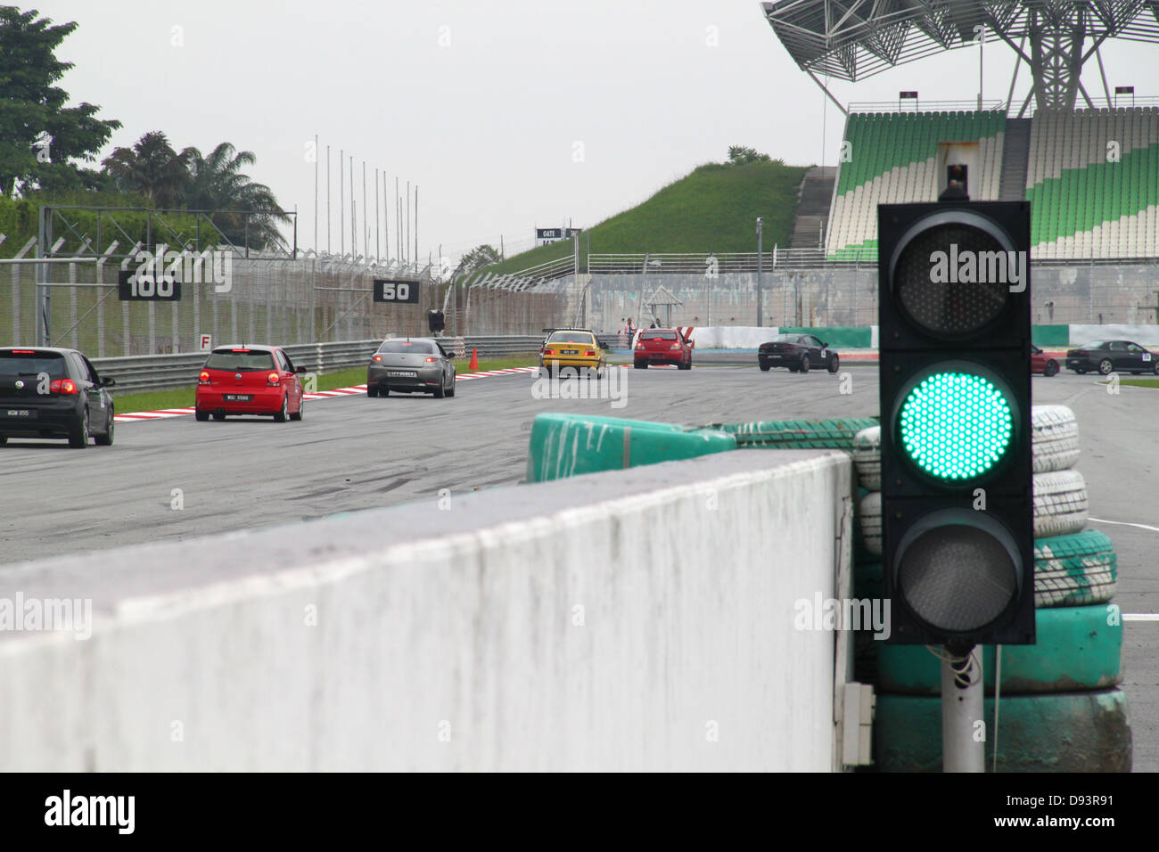 Il semaforo verde e vetture da corsa di avvicinamento ad un angolo acuto durante un giorno in pista sul circuito di Sepang in Malesia. Foto Stock