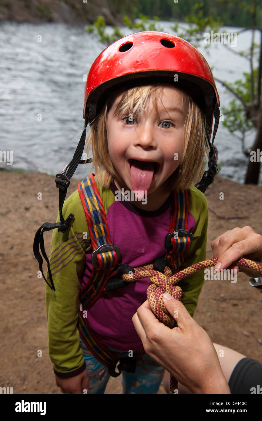 Ragazza in sport casco spuntavano lingua mentre suo padre controllando la sua attrezzatura Foto Stock
