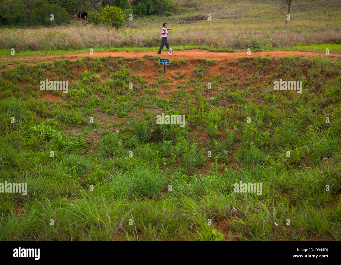 L'uomo passando davanti ad un cratere di una bomba a Pianura di giare Phonsavan, Laos Foto Stock
