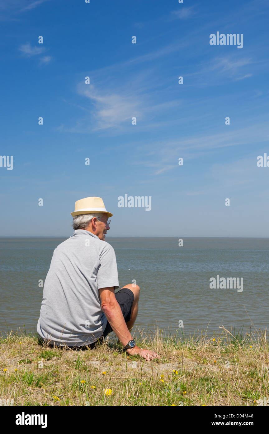 Uomo anziano è seduto sulla diga olandese in Lauwersoog Foto Stock