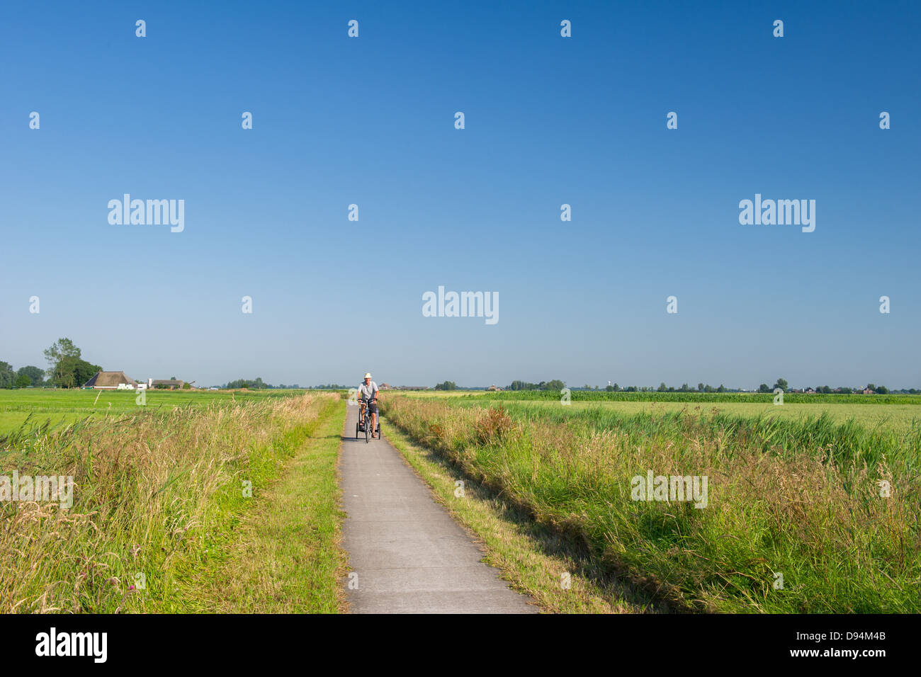 Uomo in bici con il cane trawler nel paesaggio olandese in Frisia Foto Stock