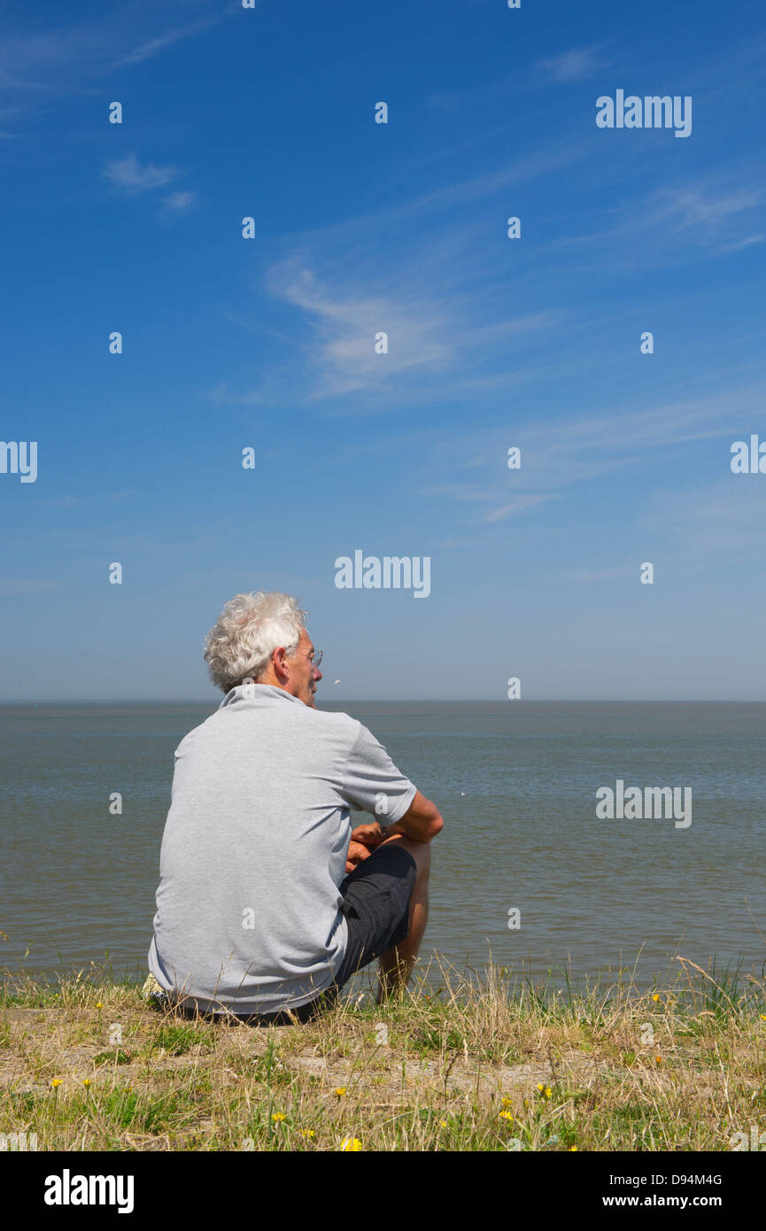 Uomo anziano è seduto sulla diga olandese in Lauwersoog Foto Stock
