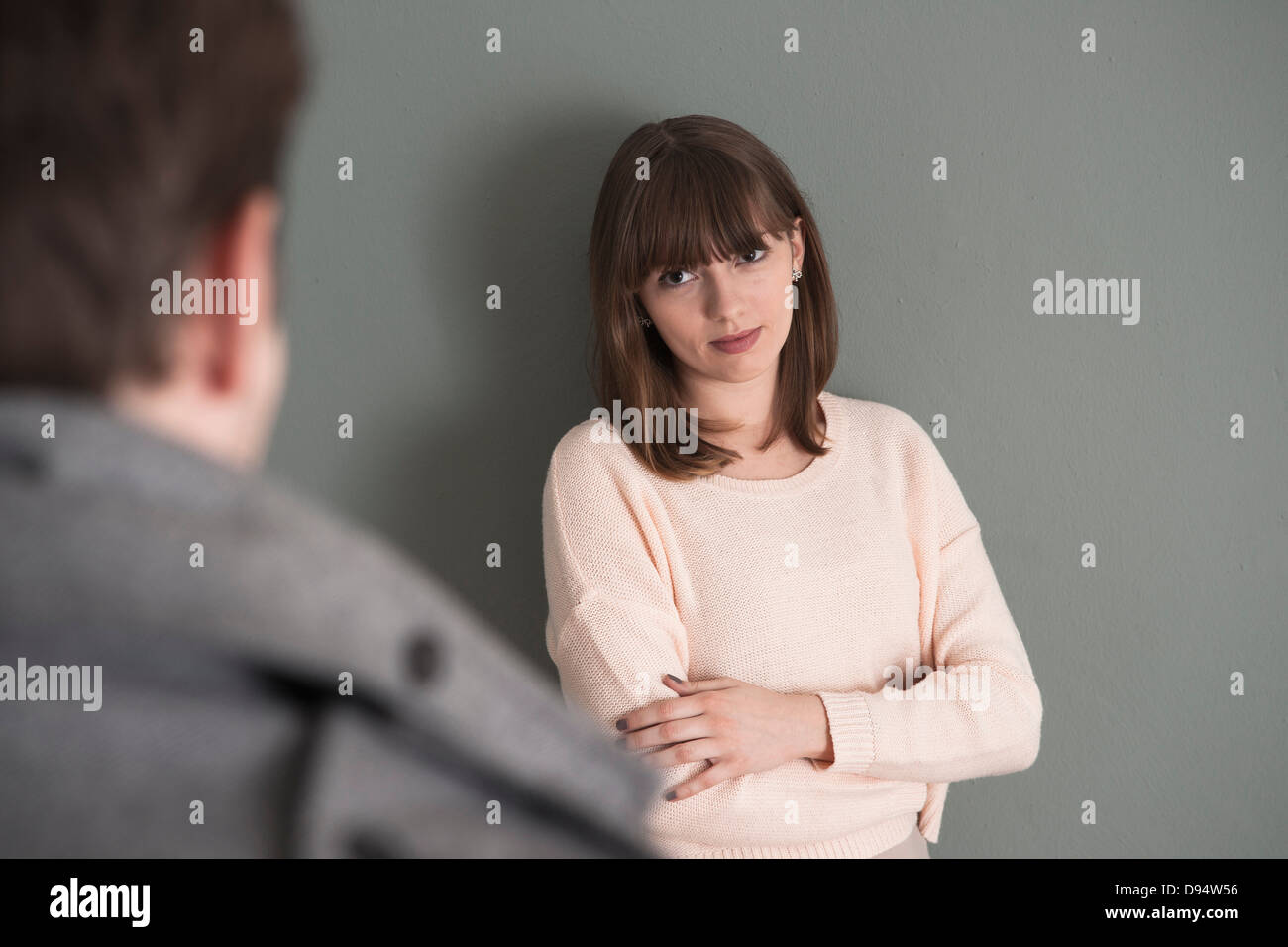 Ritratto di giovane donna in piedi nella parte anteriore del giovane uomo, guardando a lui intensamente, Studio shot su sfondo grigio Foto Stock