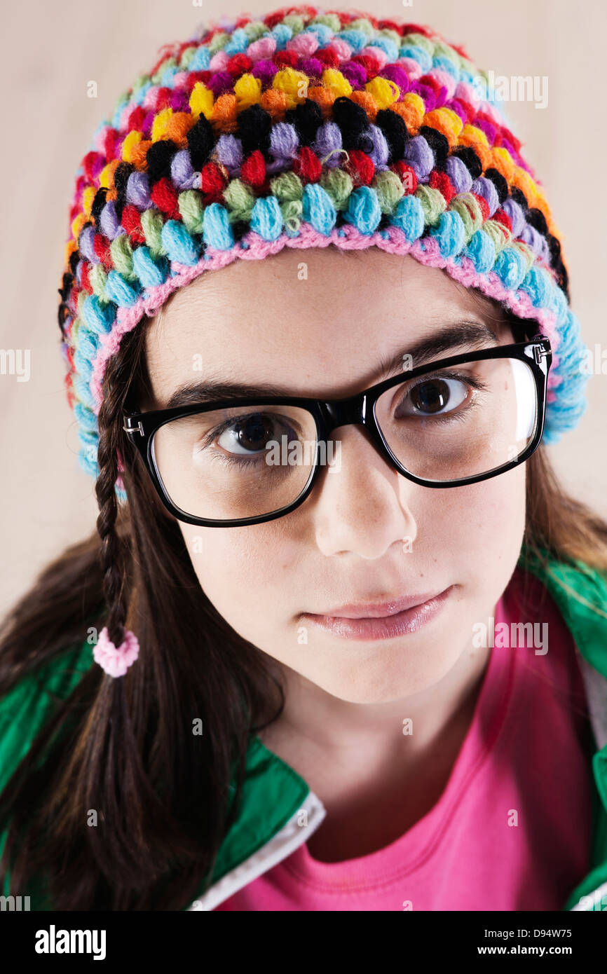 Close-up verticale di una ragazza che indossa Cappello di lana e il Corno-bordati di occhiali, guardando la telecamera, Studio shot su sfondo bianco Foto Stock