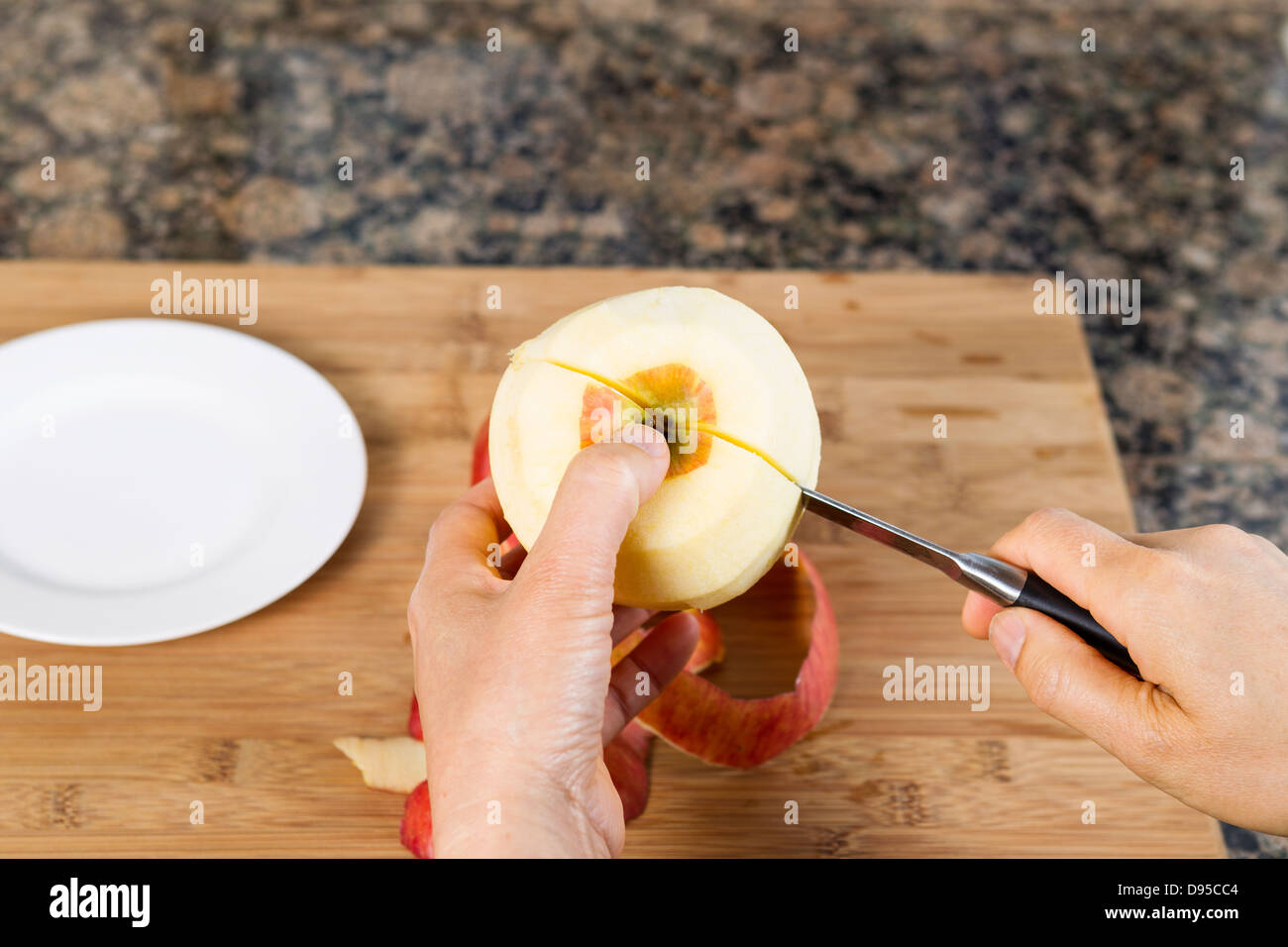 Mani femminili di taglio mela sbucciata a metà con coltello seghettato con bambù tagliere e banco di cucina in background Foto Stock
