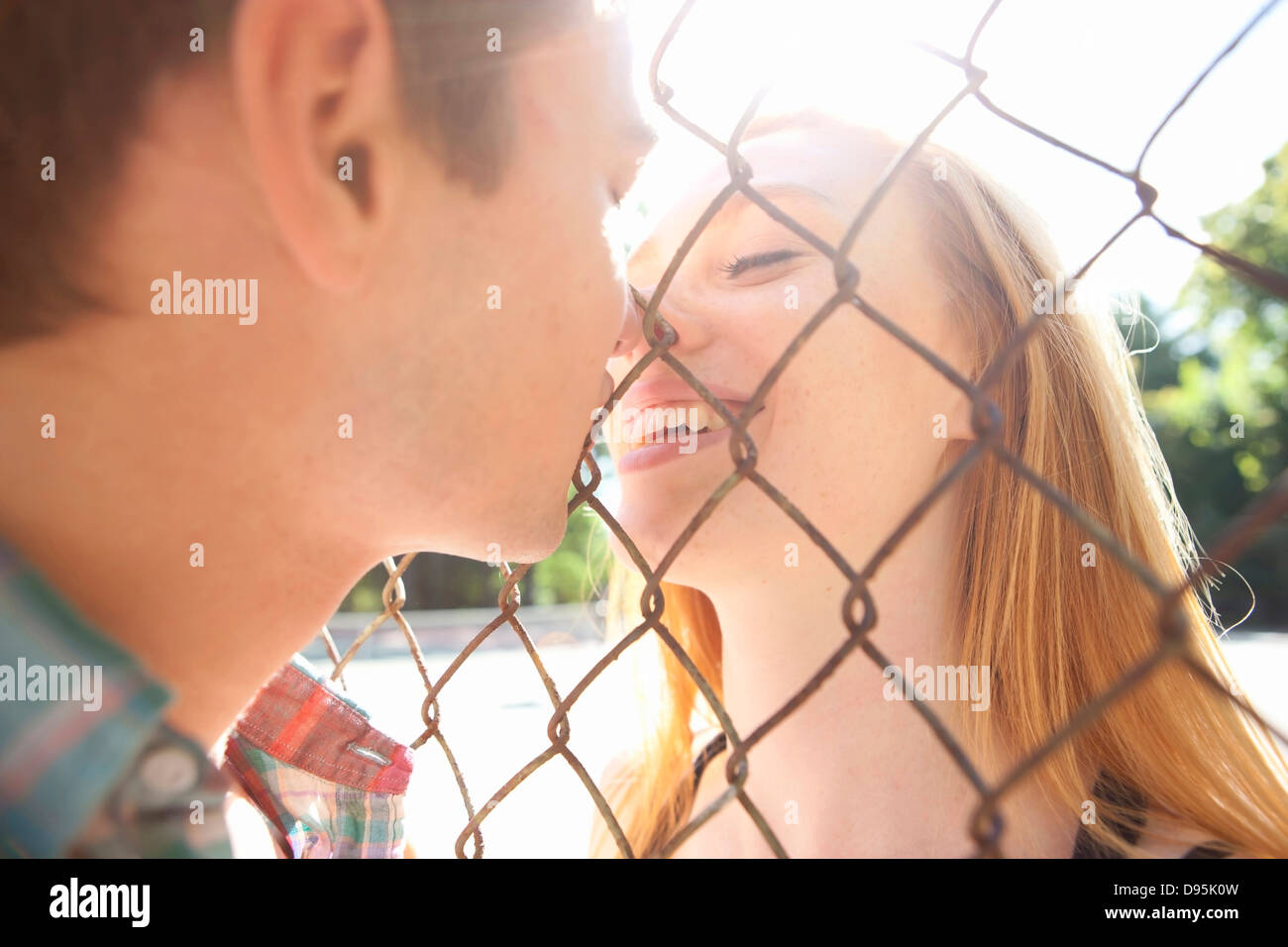 Coppia giovane kissing attraverso la catena collegamento recinto nel parco vicino al campo da tennis in una calda giornata estiva a Portland, Oregon, Stati Uniti d'America Foto Stock