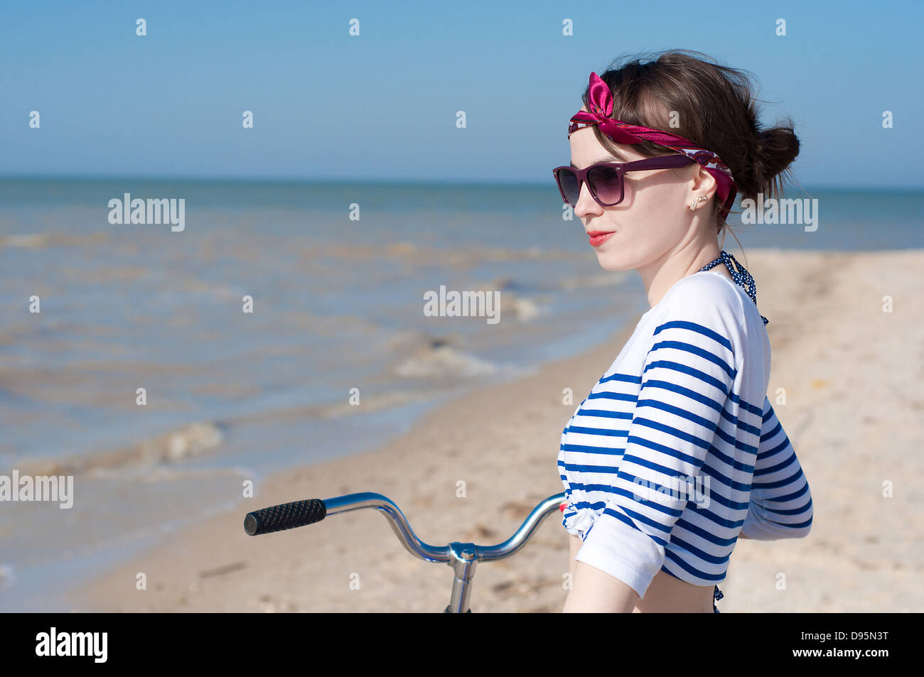 La bellissima ragazza con la bicicletta sulla passeggiata a mare contro il cielo blu Foto Stock