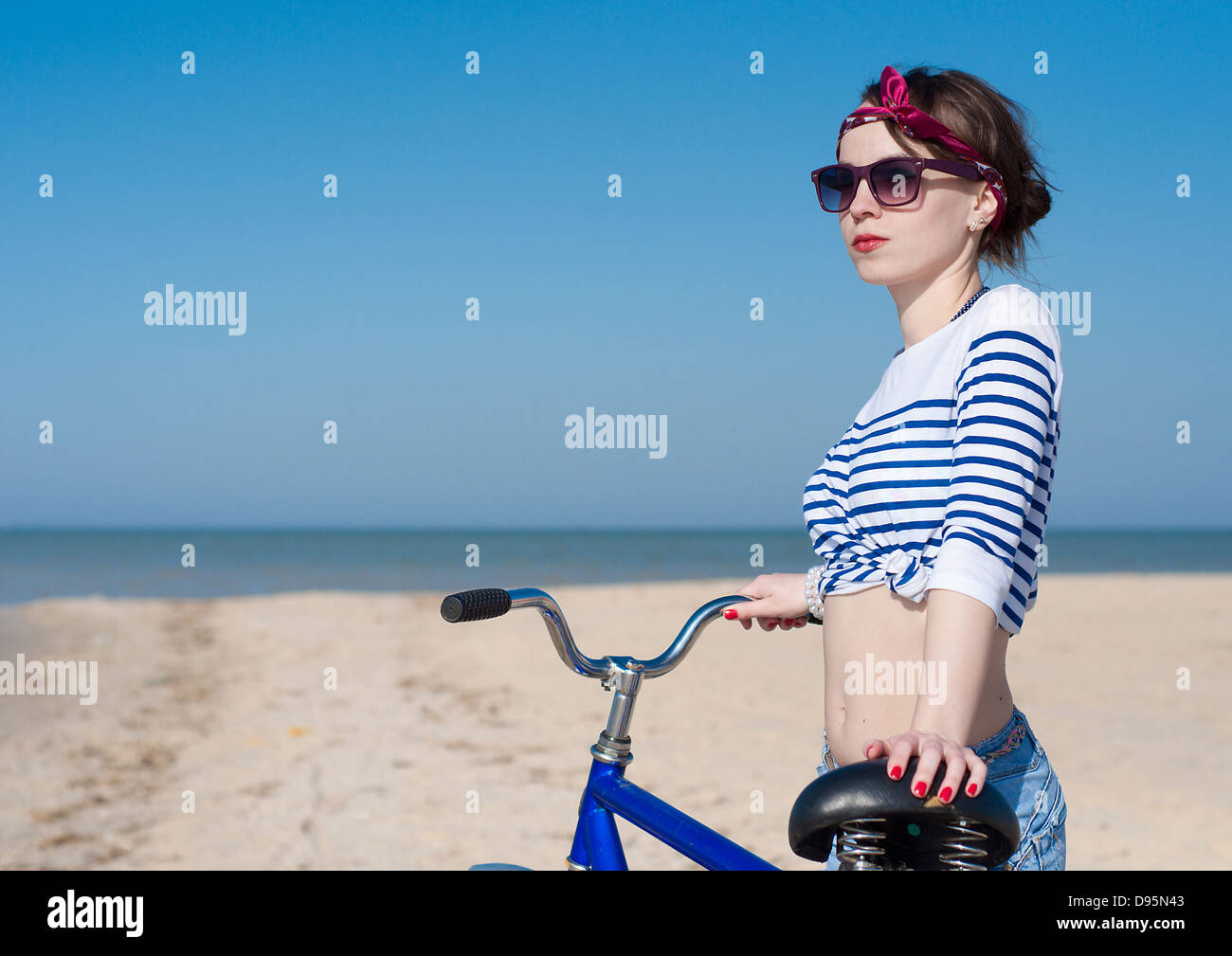 La bellissima ragazza con la bicicletta sulla passeggiata a mare contro il cielo blu Foto Stock