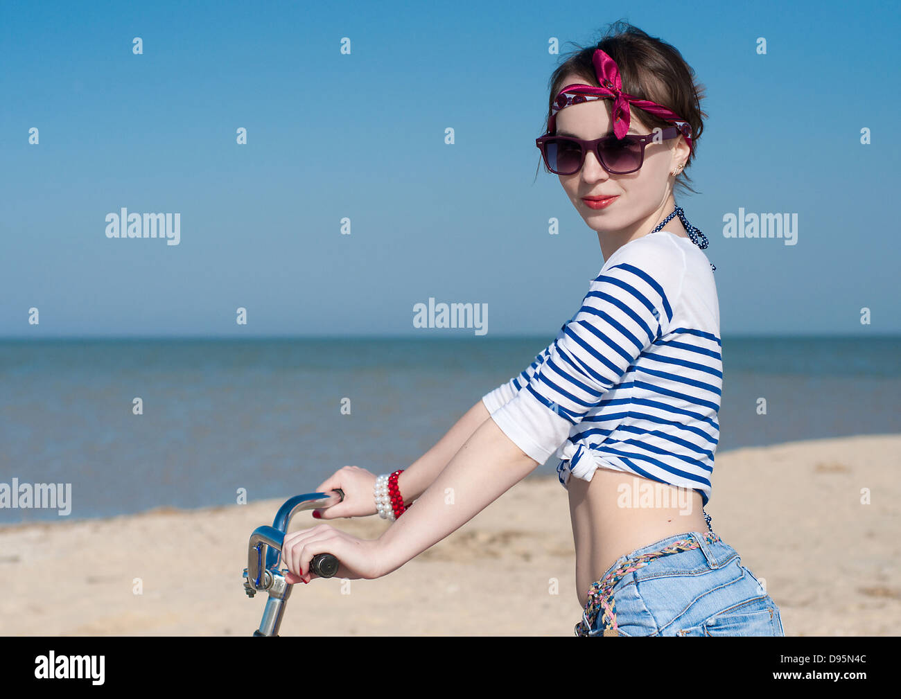 La bellissima ragazza con la bicicletta sulla passeggiata a mare contro il cielo blu Foto Stock