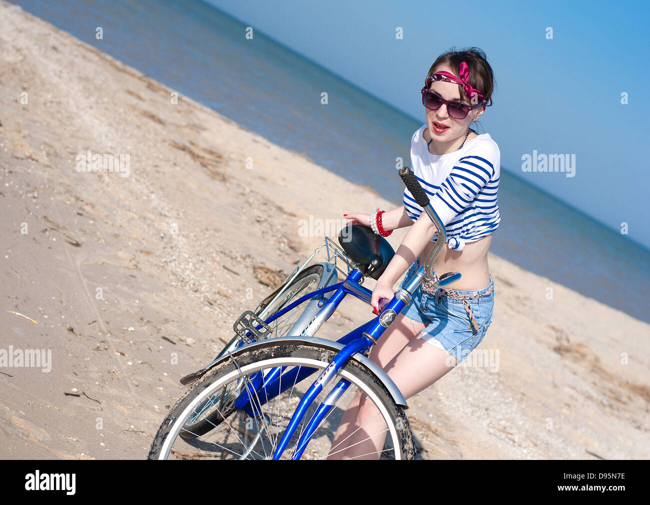La bellissima ragazza con la bicicletta sulla passeggiata a mare contro il cielo blu Foto Stock